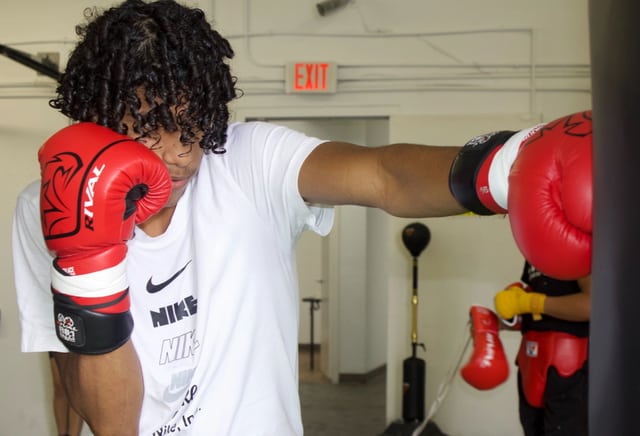 A boxer wearing red gloves practices a punch in the gym.