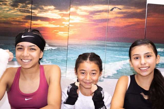 Three people with boxing hand wraps pose together at the gym.